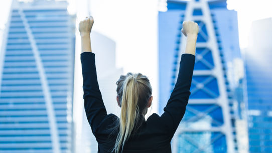 A behind shot of a woman with her hands up in celebration with a backdrop of a city skyline