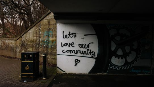 Underneath an overpass with graffiti on the wall saying "Lets love our community"