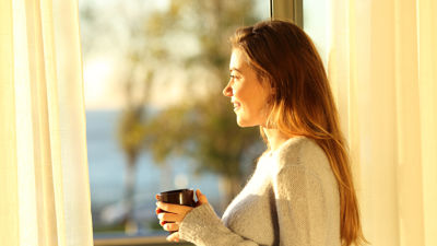 A woman holding a mug looking out the window during golden hour
