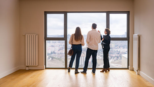 A property manager with a couple looking out the window of an empty apartment