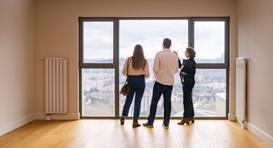A property manager with a couple looking out the window of an empty apartment