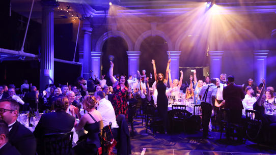 A group standing up in celebration at their table at a property managers industry event